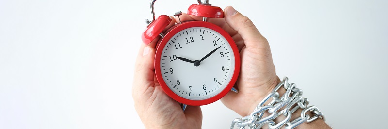 Male hands are tied with chain and hold red alarm clock. Chronic fatigue insomnia and deadlines concept