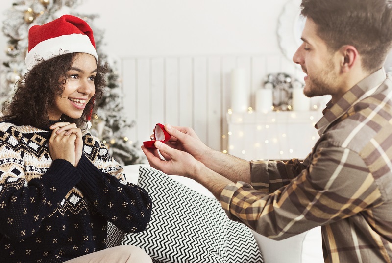Christmas proposal. Handsome man giving engagement ring to excited black woman, copy space